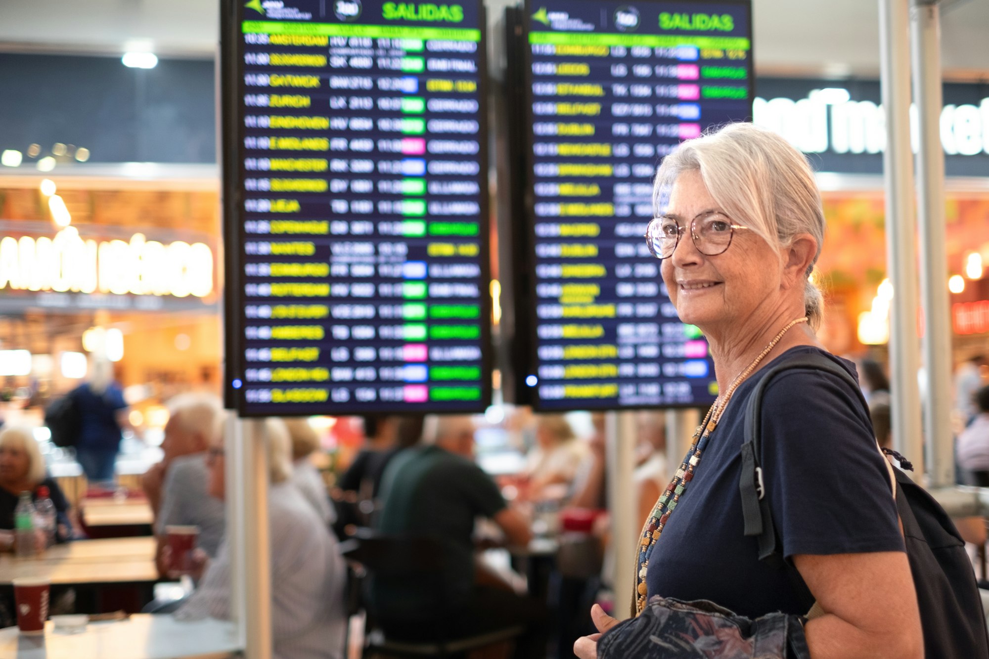 Woman traveler - senior lady standing inside airport terminal looking at timetable schedule