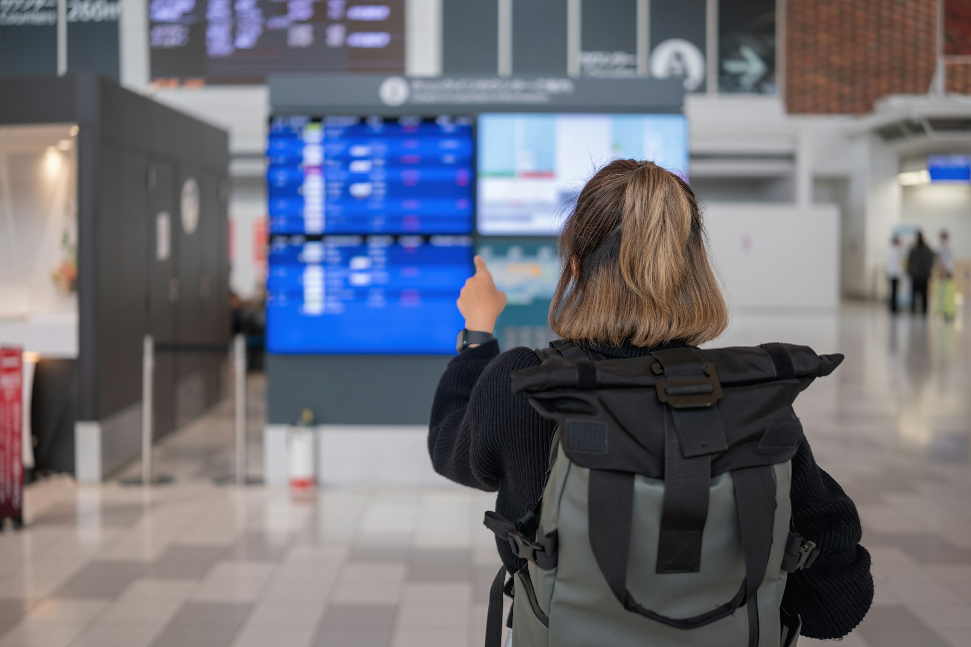 Young Asian woman in international airport looking at flight information board, checking her flight